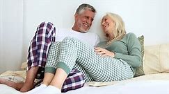 Mature senior couple in pajamas lying in bed flirting and playing jokes together