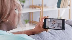 Young woman patient talking online to female friendly doctor from home during video call using mobile phone. Girl having medical consultation by virtual webcam. Telemedicine concept. 4k video.