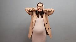Irritated emotional pregnant woman wearing dress jacket and glasses isolated over gray background screaming loud covering ears with hands suffering from obsessive noise