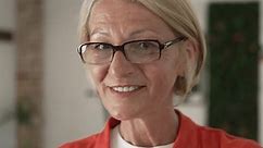Portrait of one mature blonde caucasian woman with eyeglasses at home or office happy smile looking to the camera confident wear sweater in bright room slow motion