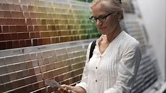 Closeup of smiling mature woman comparing color swatches at a paint display shopping for home redecorating renovation project, in a hardware store.