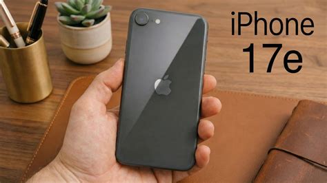 Visão traseira de um smartphone iPhone 17e na cor cinza espacial sendo segurado por uma mão, destacando a câmera única e o logotipo da Apple.