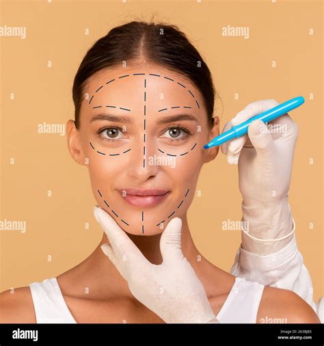 Plastic surgeon drawing marks on young woman's face for cosmetic surgery operation on beige ...