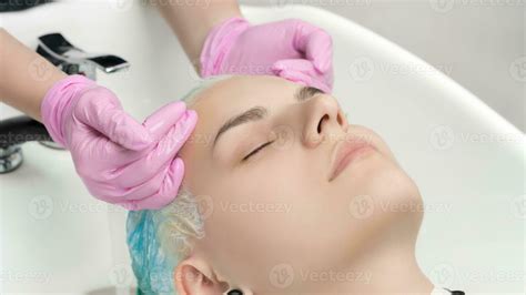 Hairstylist hands in pink gloves washing hair of young woman in ...