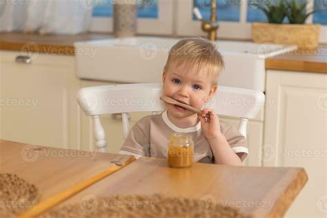 Happy family at home. Baby boy feeding himself in kitchen. Little boy with messy funny face eats ...