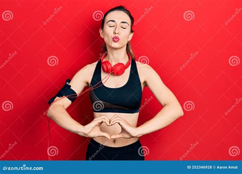 Young Hispanic Girl Wearing Gym Clothes and Using Headphones Doing Heart Symbol with Hands ...