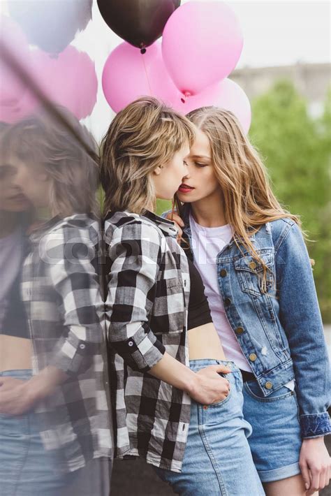 young casual lesbian couple kissing and holding air balloons outdoors ...