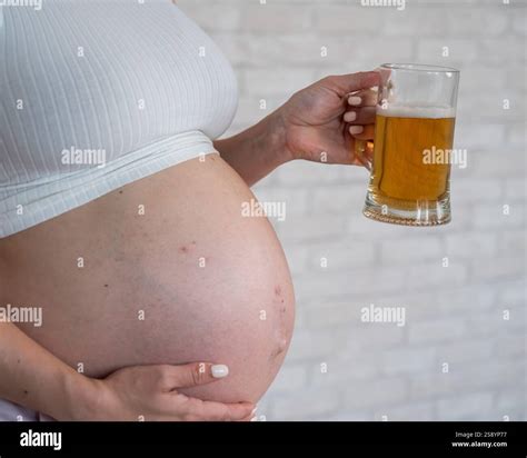 Faceless pregnant woman with rash on stomach holding glass of beer ...