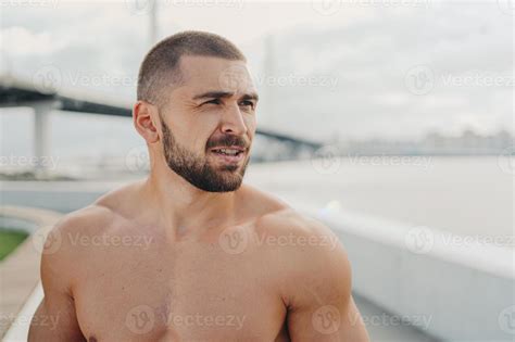 Outdoor shot of bearded man with muscular naked torso concentrated into ...