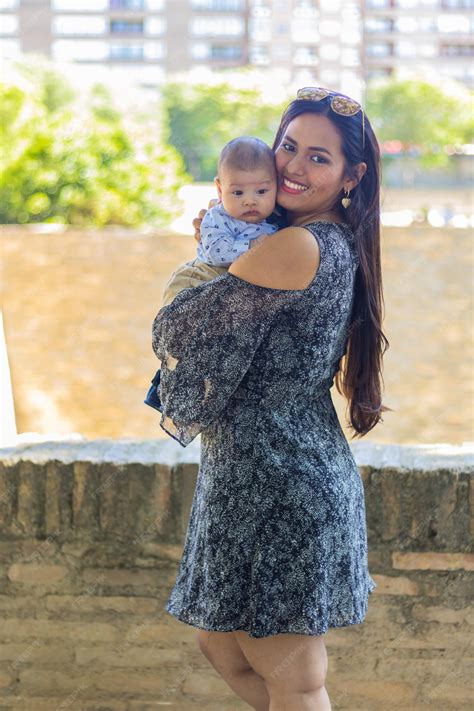 Premium Photo | Beautiful latina mom with her baby in her arms in a city park wearing a black ...