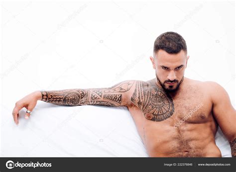 Nude male model lies in white bed. Muscular tattooed Man ready to St ...