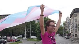 A bigender man holding his arms up high as he holds a transgender...