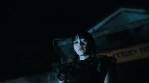 Creepy girl in gothic attire standing under a haunted house sign at night.