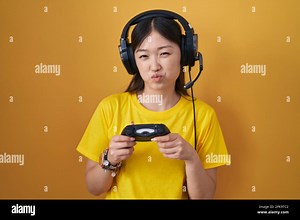 Chinese young woman playing video game holding controller puffing cheeks with funny face. mouth inflated with air, crazy expression Stock Photo - Alamy
