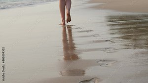 Woman walk along beach, leave footsteps on wet sand, low camera show how she go away. Sea wave splash at shore and water touch traces, then move back and quickly absorb in sand