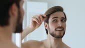 Mirror reflection happy handsome man styling hair with comb,...