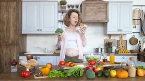 Junk Food vs Healthy Food. Pregnant Woman Holding Burger And Broccoli Deciding What To Eat.