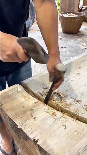A craftsman chisels a deep groove into a wooden beam using steady hammer strikes