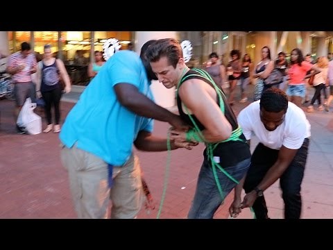Two Guys Tie Up Man On Street While Police Watch