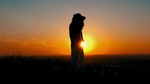 silhouette girl standing on the hill looking on amazing sky with rising sun female skirt and hair fluttering on the wind