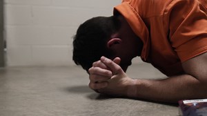A prison inmate lays on ground crying, praying, weeping, sobbing next to bible while wearing orange prison uniform jumpsuit | Premium Stock Video Footage