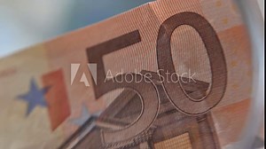Euro banknotes being inspected with a magnifying glass. The magnification highlights intricate security features, micro-printing, and detailed textures, creating an analytical financial scene Stock Video