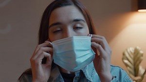 Woman putting on face mask looking into lens