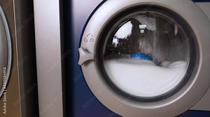 Industry washing machine washes dirty colorful clothes. Washing clothing in domestic washing machine. Close up video of spinning drum washing machine.