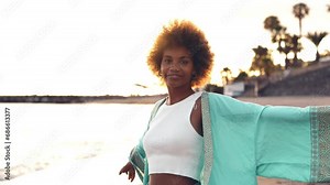 One young beautiful afro woman walking on the sand of the beach enjoying summer and having fun outdoors with sunset in the background. People vacations free time concept enjoy
