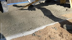 A cement rake is used by building construction workers in rubber boots, to spread wet concrete that is pouring out of the chute from the mixer truck. Stock Video