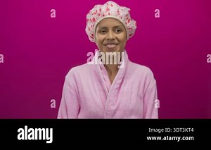 Young hispanic woman in bathrobe with shower cap stands against isolated pink wall with surprised expression, embodying everyday skincare routine in a vibrant setting Stock Video Footage - Alamy