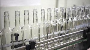 Filling of alcohol in glass bottles at the plant. Conveyor close-up. The production process of alcoholic beverages. Conveyor belt with glass bottles.