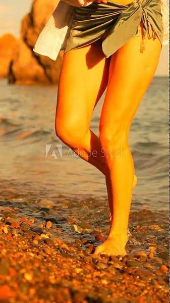 Legs, beach, walking woman's bare legs on a pebble beach at sunset, enjoying a peaceful summer vacation vertical video