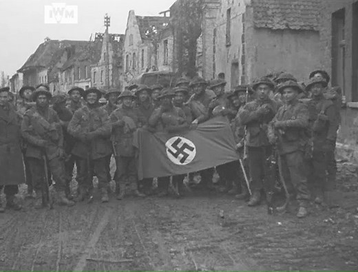 Men of the 10th Battalion, Highland Light Infantry, pose with a captured Nazi flag and sign reading Adolf Hitler-Strasse in Kranenburg, Germany, February 1945. Film: IWM A70 239-2 | Imperial War Museum London