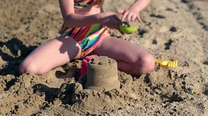 Little girl playing with sand on beach ocean sea. Childhood and summer vacation concept. Smiling child having fun outdoors on family holidays. Kid building sand castle. Trip to warm countries
