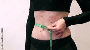 Girl measures her waist with a tape measure. Girl with a tape measure in her hands. Concept of losing weight, diet and weight control. Body volume control. Girl measures her figure after losing weight