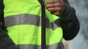 Close-up view of unzipped high visibility safety vest in fluorescent yellow with silver reflective stripes, showing detailed black zipper and textured dark inner clothing, designed for protective outdoor | Premium Stock Video Footage