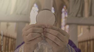 Chaplain lifting communion bread from golden plate on altar close up. Christian priest holding sacramental host in hands during Holy Communion ceremony ritual