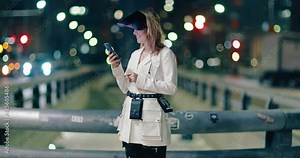 Smiling blonde woman wearing trendy COVID face shield at central city street, looking on screen of her smartphone. Pretty young woman in stylish white jacket with night scene downtown on background 4K