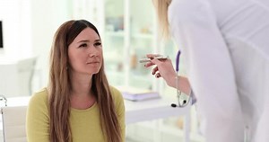 Young woman at appointment with neurologist. Female doctor checking eye reflexes with flashlight in clinic