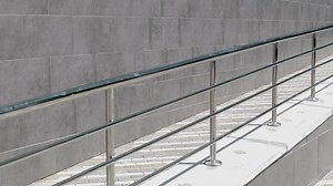 A ramp with stainless steel handrails for wheelchairs, bicycles and strollers with children in front of the building. Handrail for lifting a wheelchair. Shiny stainless steel handrail.