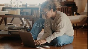Adult woman browsing the net using a laptop computer sitting on the floor at home in indoor technology online activity. Searching the web. Female people messaging or email sending. Small business