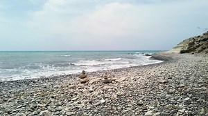 Pebble-covered beach in Pissouri, Cyprus, with two balanced stone stacks near the shoreline. Gentle waves and natural coastal scenery, ideal for nature, travel, and meditative themes. | Premium Stock Video Footage
