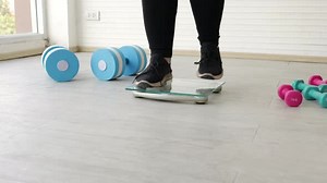 Person Weighing Themselves with Dumbbells on Floor