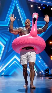 What’s The Rock doing in a pink flamingo float on AGT? The answer will leave you speechless. Full video below in the comments. | Adama Paris