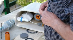 A plumber repairman takes out an old cistern fittings from a dirty rusty toilet tank and brings it to the camera. Plumbing blockages due to dirty and hard water. Repair