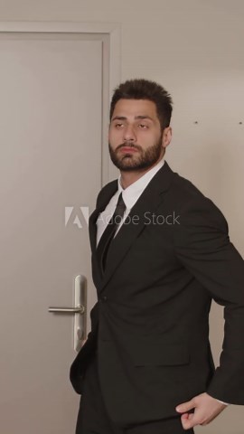 Vertical medium shot of handsome young Middle Eastern male entrepreneur on business trip entering hotel room and looking around wearing elegant formal suit and tie