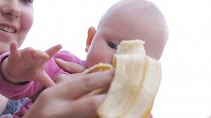 Baby eating banana from hands of mother