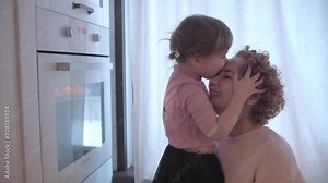 Little girl fooling around in the kitchen. Mom and daughter have fun together. Mom is circling her daughter. The girl is crawling around mom. Mom and daughter have fun in the kitchen.