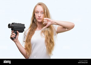Blonde woman teenager filming holding super 8 video camera with angry face, negative sign showing dislike with thumbs down, rejection concept Stock Photo - Alamy